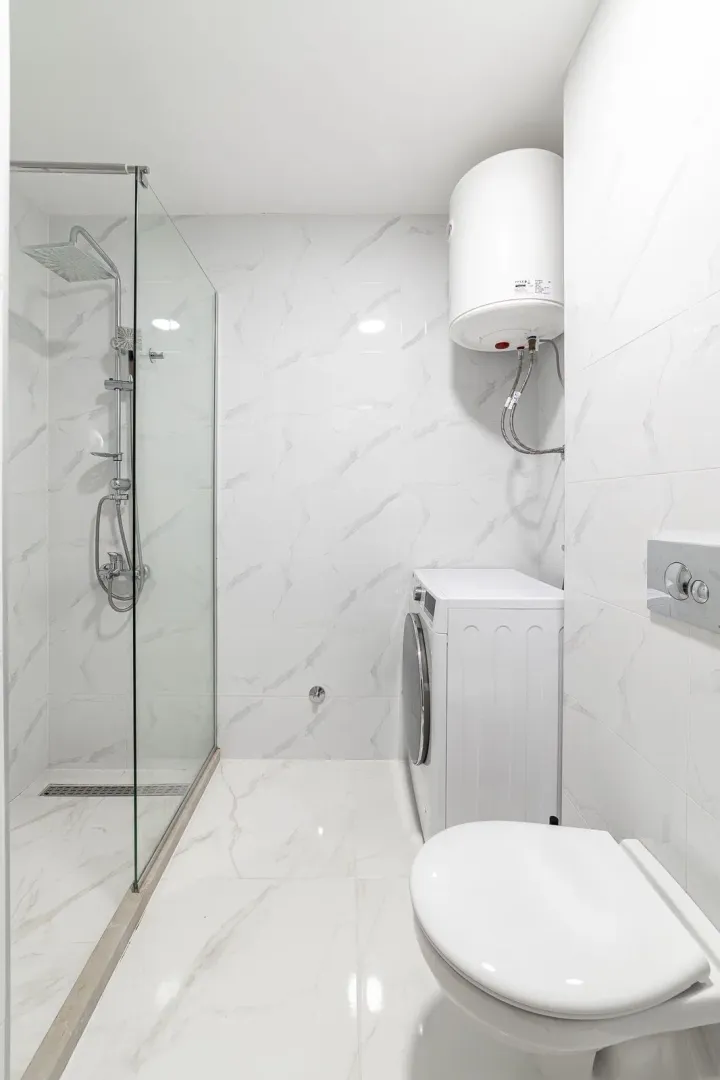 Moderne svijetlo kupatilo sa tuš kabinom, wc šoljom i veš mašinom.