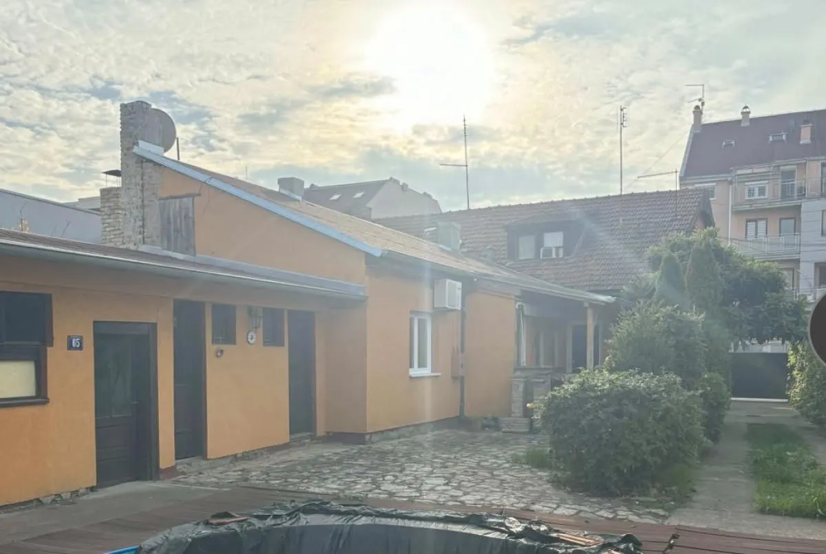 Pogled na dvorište i spoljašnjost prizemne kuće sa popločanim delom.