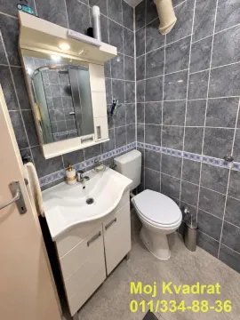 Compact bathroom with a sink, mirror, and toilet, tiled in grey. - image 14