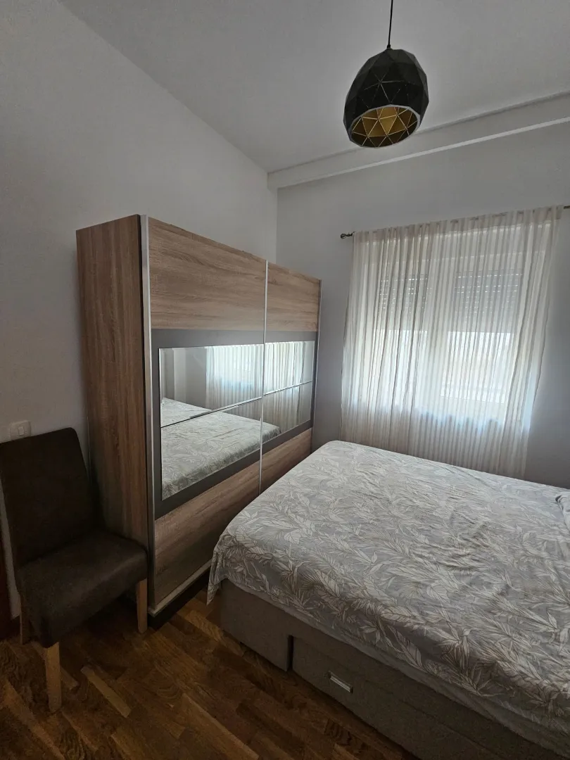 Furnished bedroom with a double bed, large wardrobe, and window with curtains.