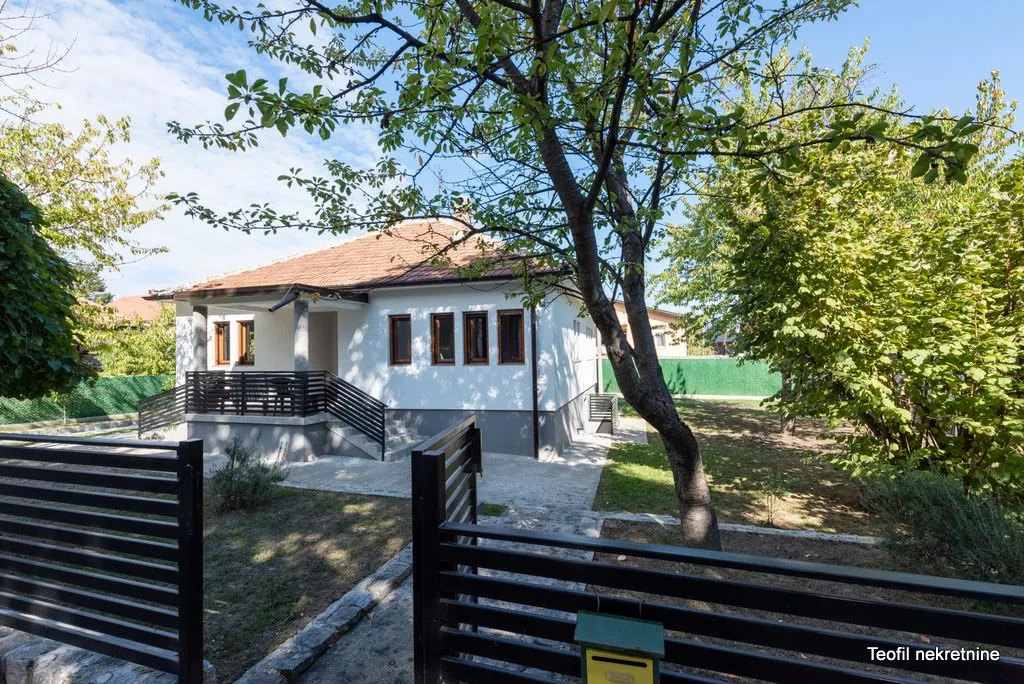 Pogled na dvorište i prednju fasadu kuće sa uređenom ogradom i zelenilom.