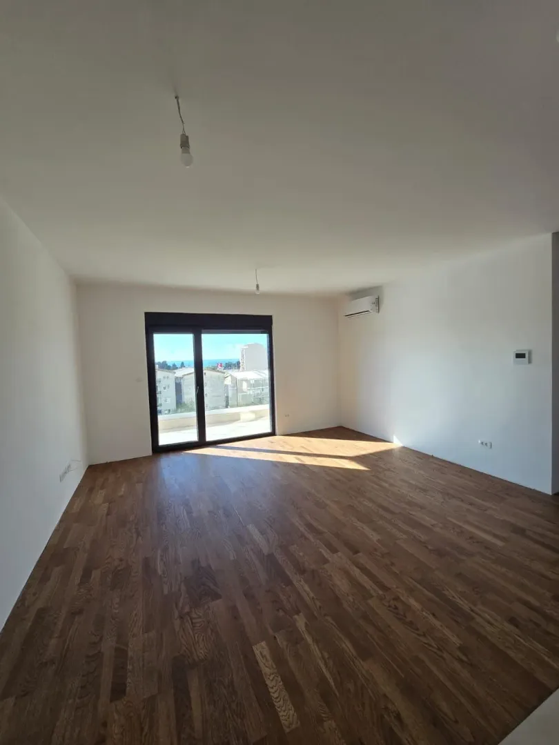 Prazna soba sa drvenim podom i izlazom na balkon.