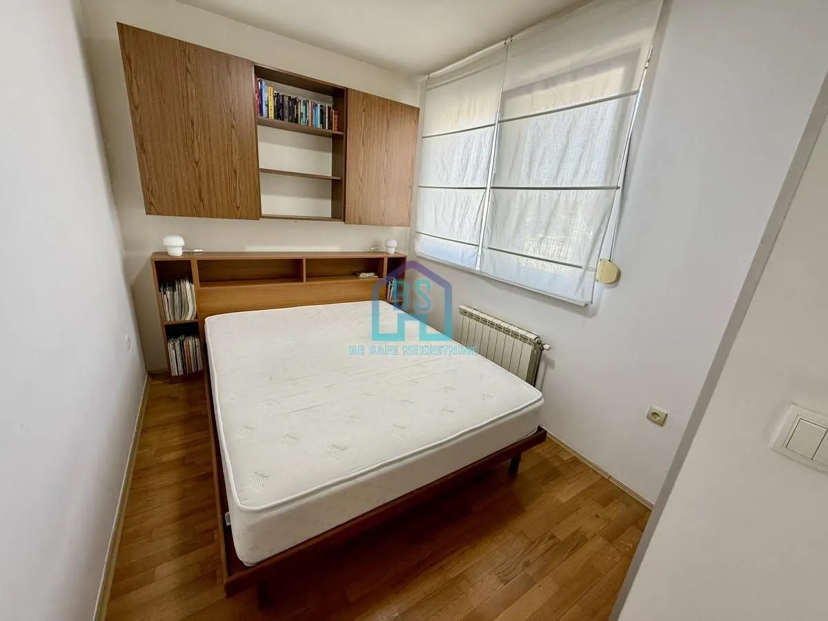 Manja spavaća soba sa bračnim krevetom i drvenim zidnim elementima.
