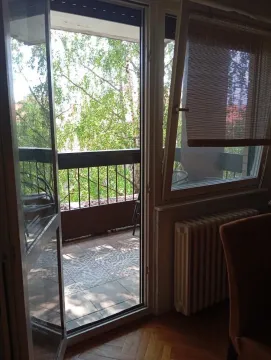 View through the open balcony door onto the terrace with furniture and greenery in the background. - image 7