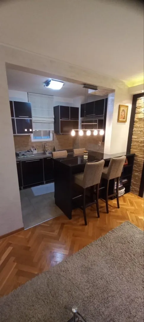 Kuhinja sa tamnim elementima i šankom sa barskim stolicama.