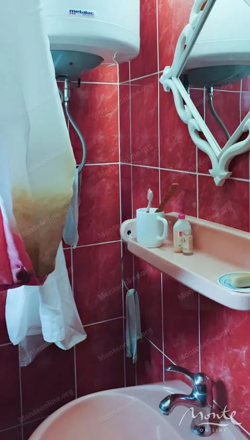 Kupatilo sa crvenim zidnim pločicama, umivaonikom i ogledalom.