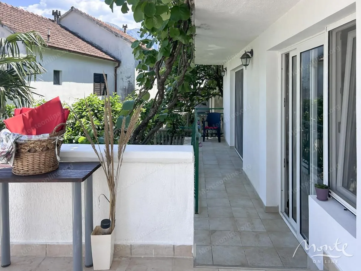 Dugački popločani balkon sa pogledom na okolno zelenilo i zgrade.