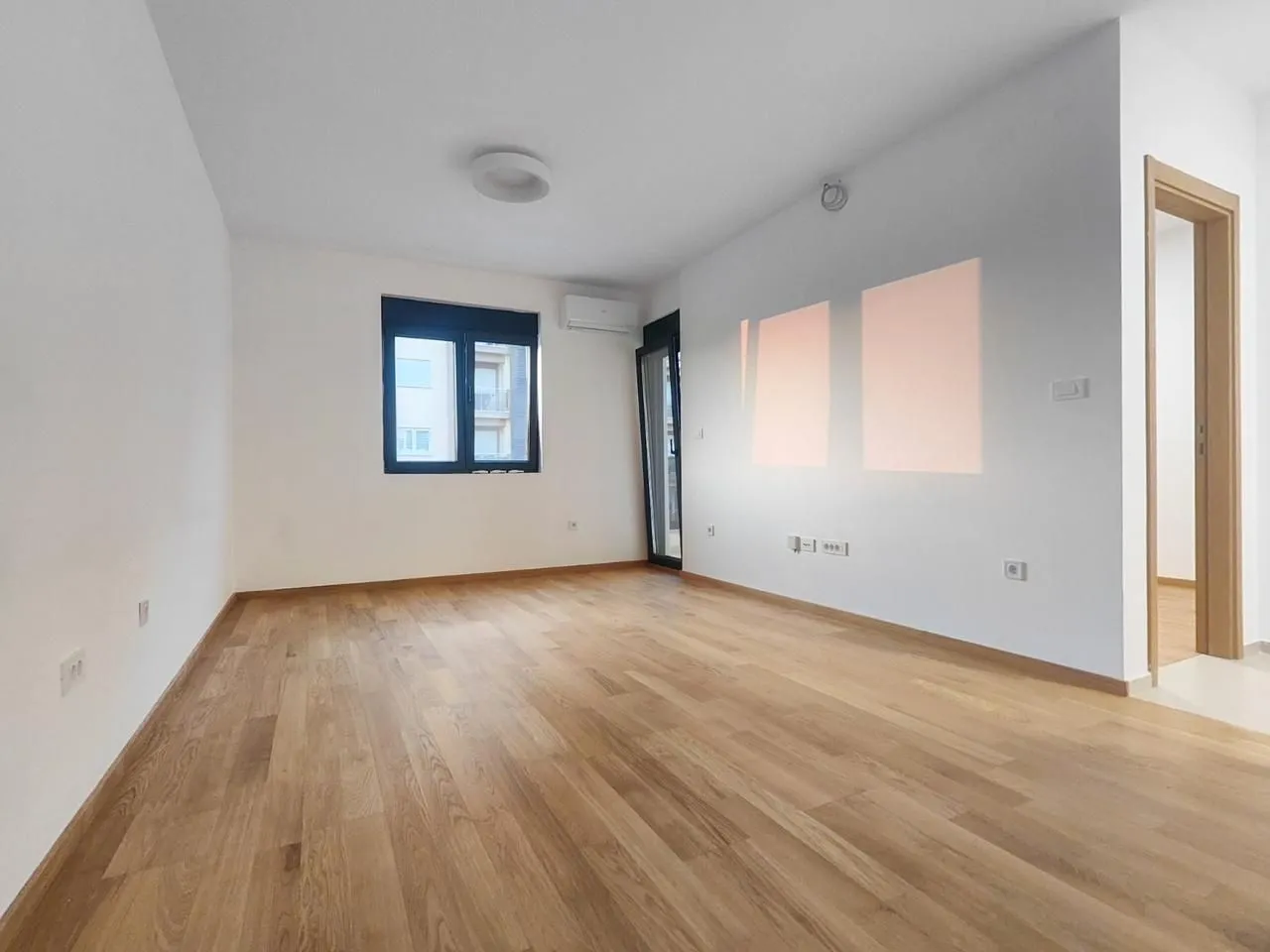Empty bright room with parquet flooring, white walls, and a window.