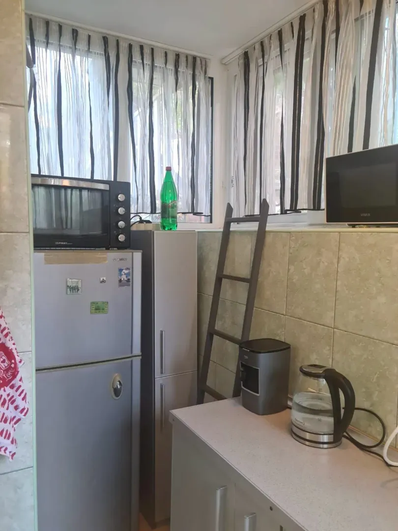 Manja kuhinja sa frižiderom, mikrotalasnom pećnicom i sudovima na radnoj površini.