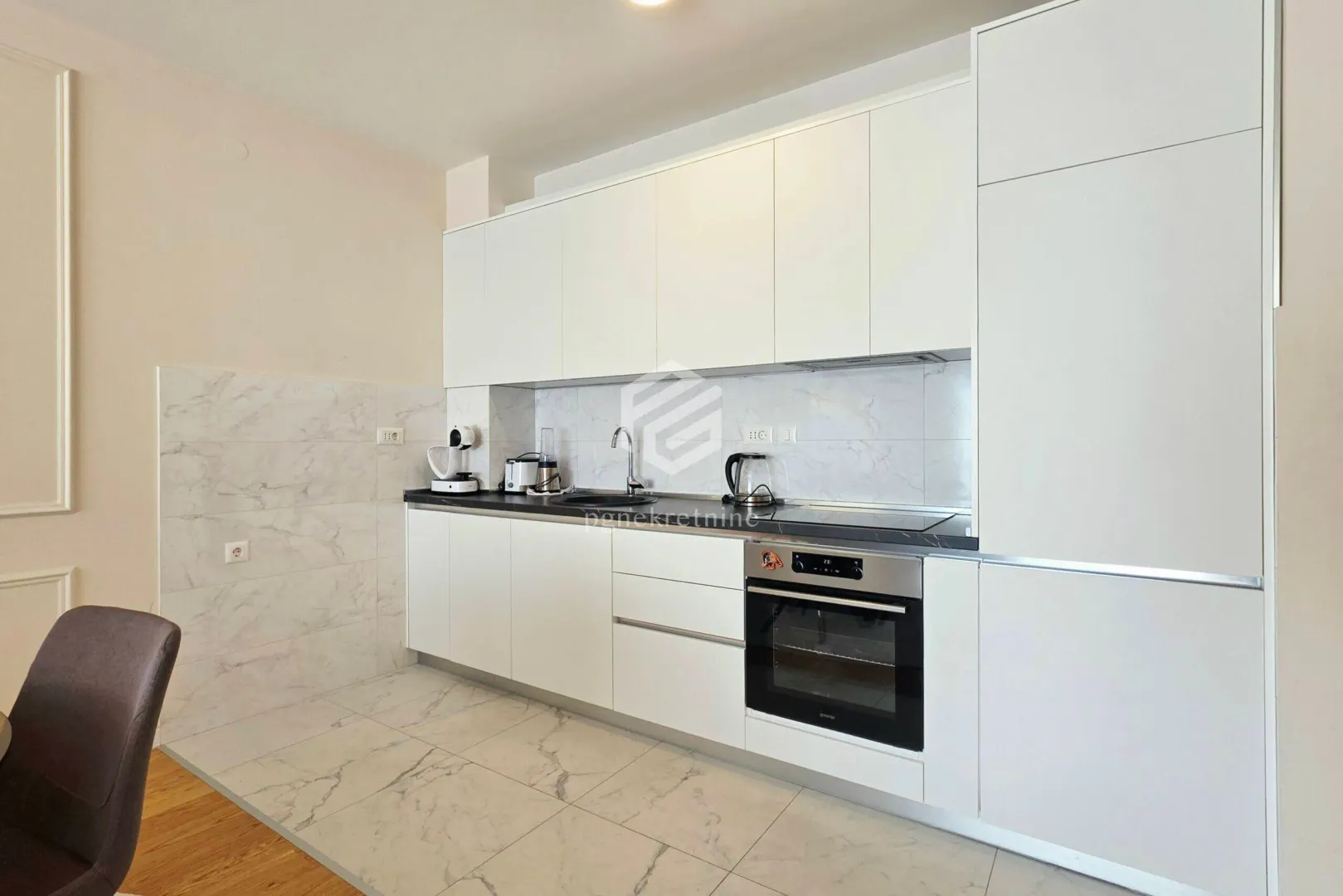 Modern white kitchen with a built-in oven and dark countertop.