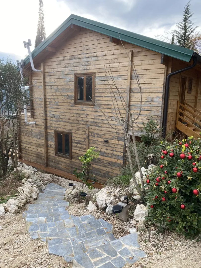 Spoljašnji izgled drvene vikendice sa dvorištem i stepeništem.
