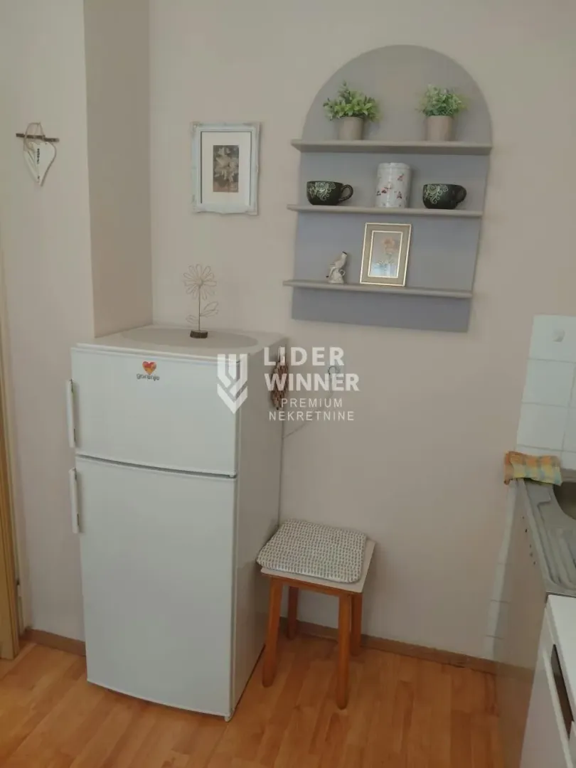 Deo kuhinje sa frižiderom, malom stolicom i zidnim policama.