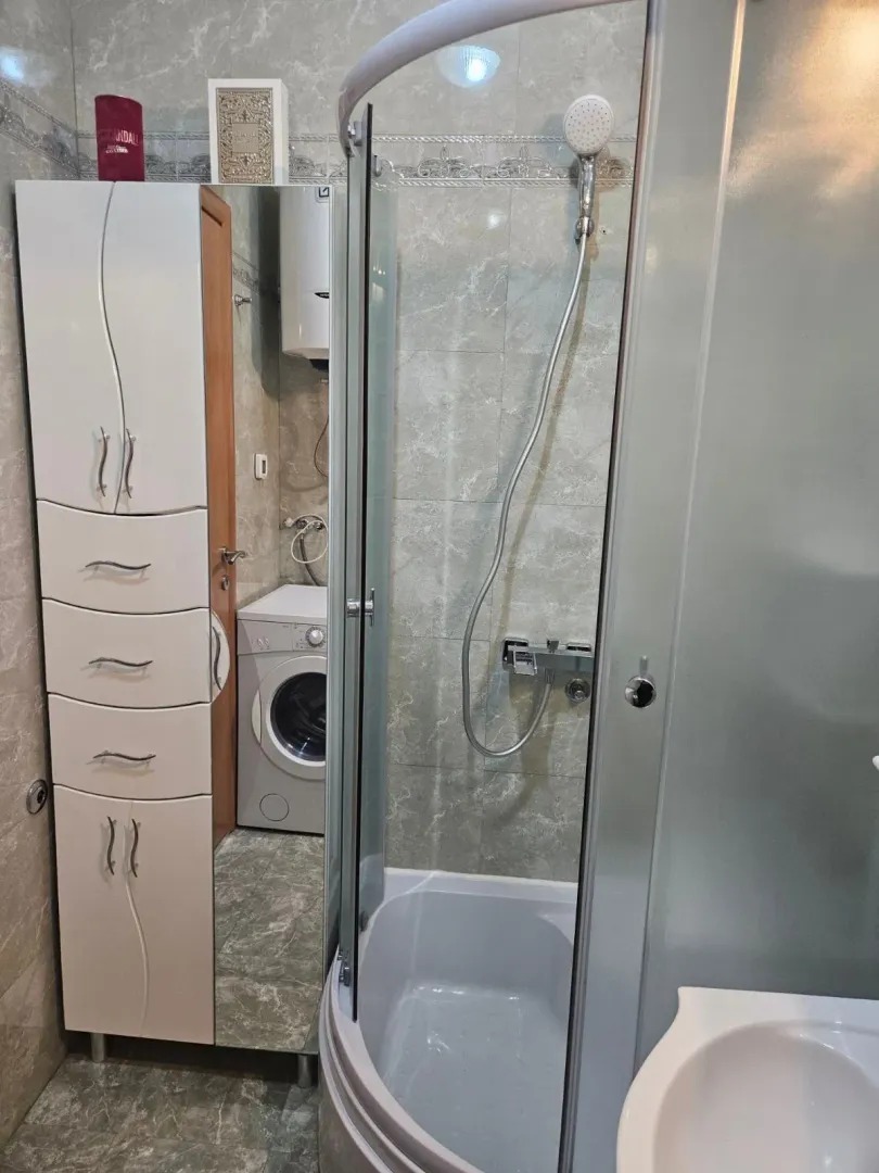 Kompaktno kupatilo sa tuš kabinom, ormarićem i mašinom za veš.