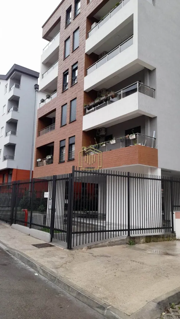 Pogled na spoljašnjost moderne stambene zgrade sa ogradom i ulazom.