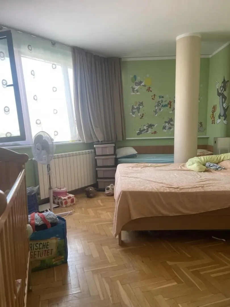 Children's bedroom with beds, parquet flooring, and a large window.