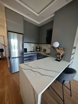 Moderna kuhinja sa šankom, trpezarijskim stolom i ugradnim elementima u sivoj boji. - image 9