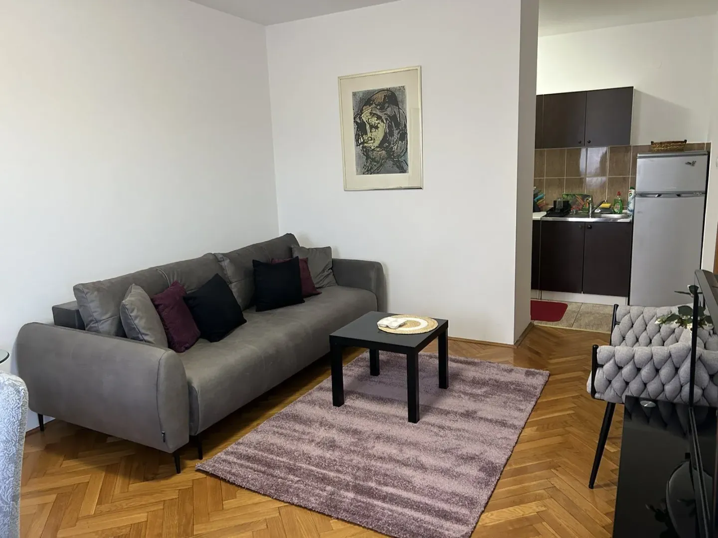 Dnevna soba sa sivom garniturom, klub stolom i kuhinjom u pozadini.
