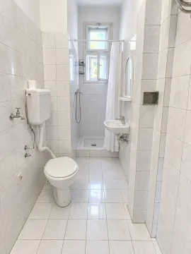 Manje kupatilo obloženo svetlim pločicama sa wc šoljom, umivaonikom i tuš kabinom. - image 8