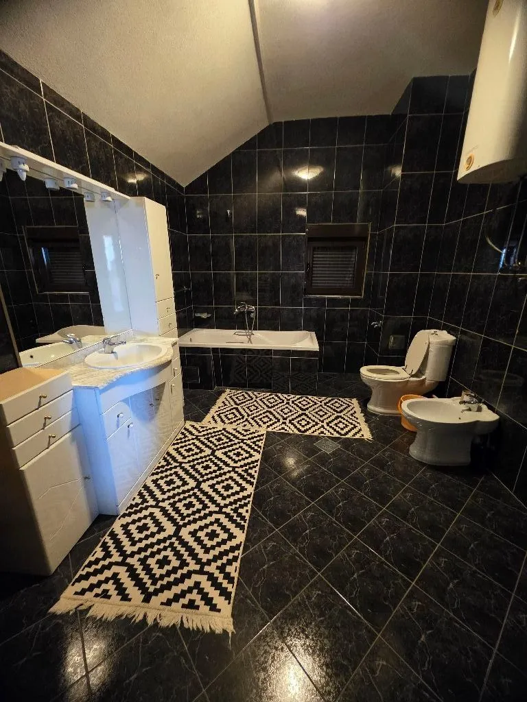 Spacious bathroom with black tiles, bathtub, sink, and sanitary fixtures.
