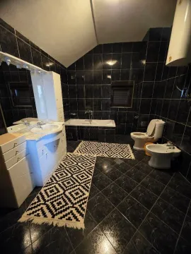 Spacious bathroom with black tiles, bathtub, sink, and sanitary fixtures. - image 15