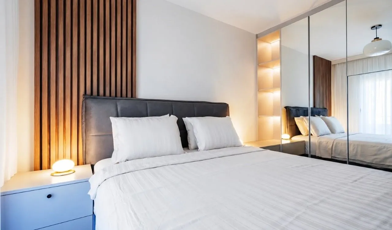 Modern bedroom with a double bed, wooden wall panel, and built-in mirrored wardrobe.