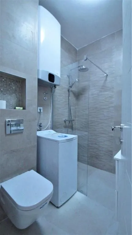 Modernly equipped bathroom with a walk-in shower, toilet, washing machine, and water heater.