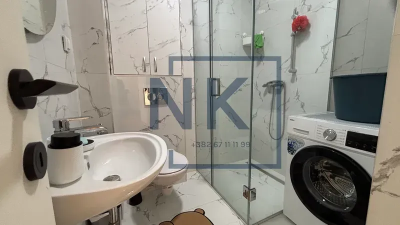 Modern bathroom with a sink, walk-in shower, and washing machine.