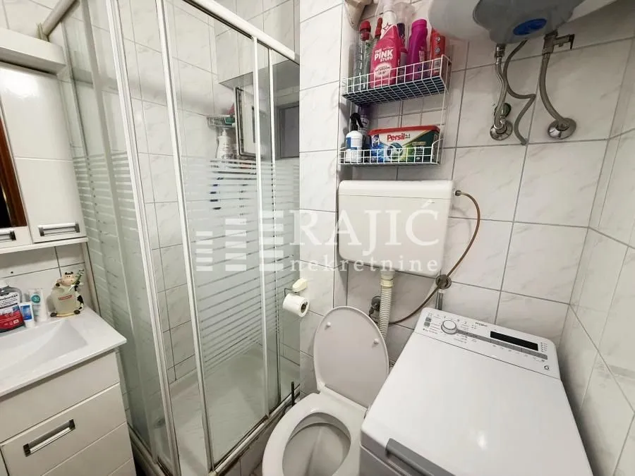 Smaller bathroom with a shower cabin, sink, toilet, and washing machine.