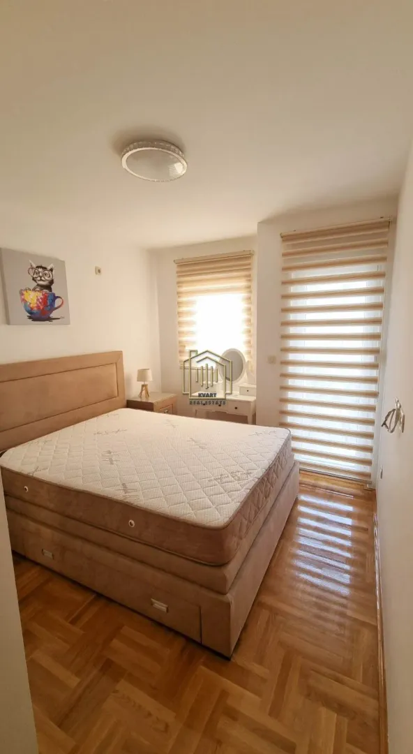 Bedroom with a double bed, wooden parquet flooring, and windows with blinds.