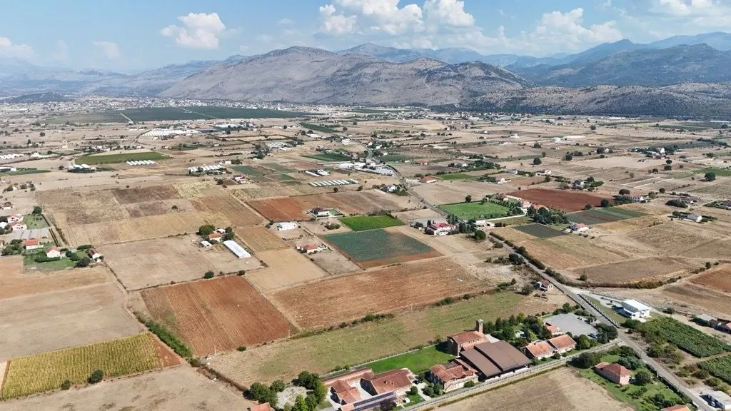 Pogled iz vazduha na seosko imanje sa poljoprivrednim zemljištem i planinama u pozadini.