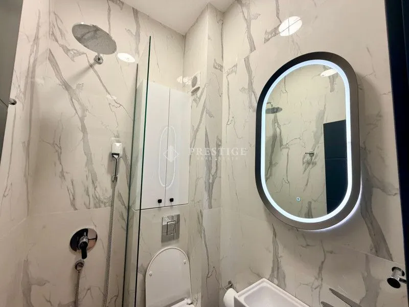 Modern bathroom with a shower cabin, white marble tiles, and an illuminated mirror.