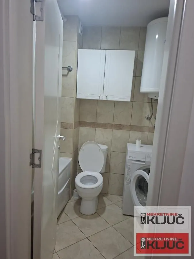 Pogled na kupatilo sa sanitarijama, ormarićem i mašinom za veš.