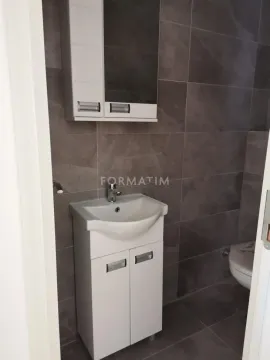 Manje kupatilo sa umivaonikom, ormarićem i toaletom obloženo tamnim pločicama. - image 4