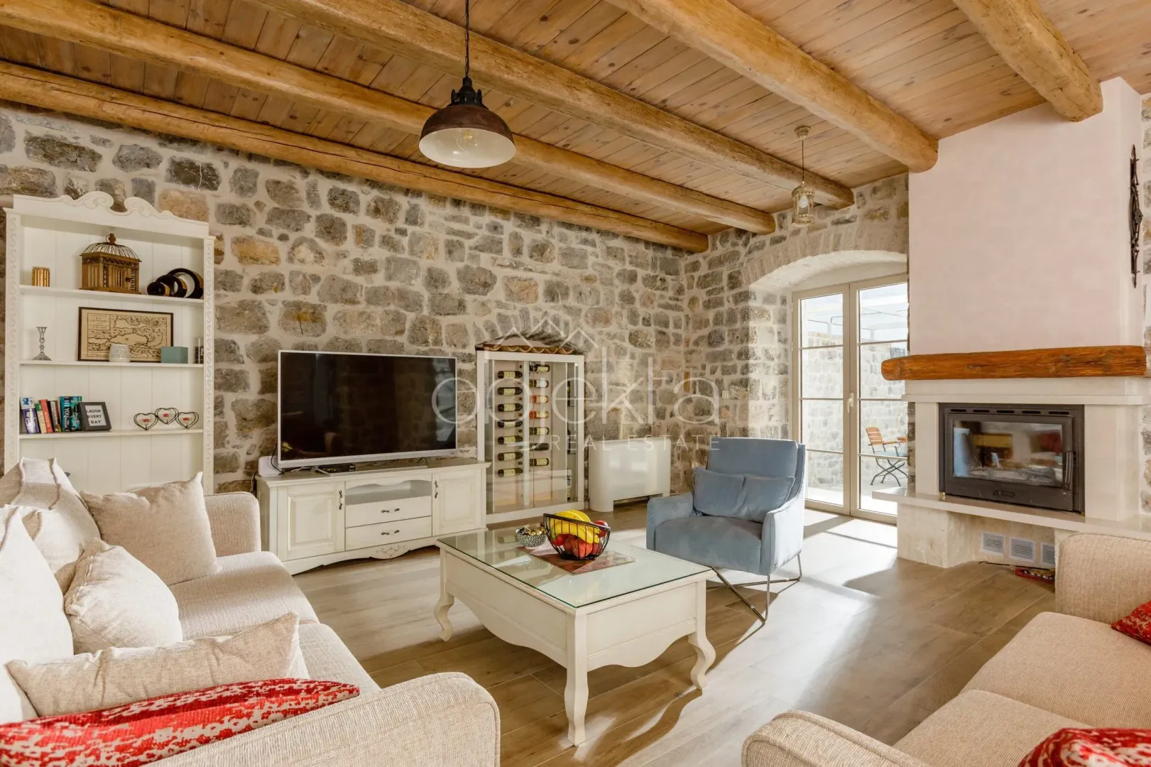 Living room with a fireplace, stone wall, and wooden ceiling beams.