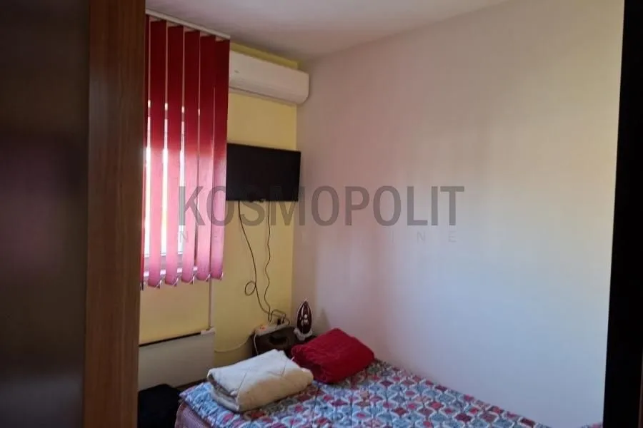 Manja spavaća soba sa krevetom, televizorom i klima uređajem.