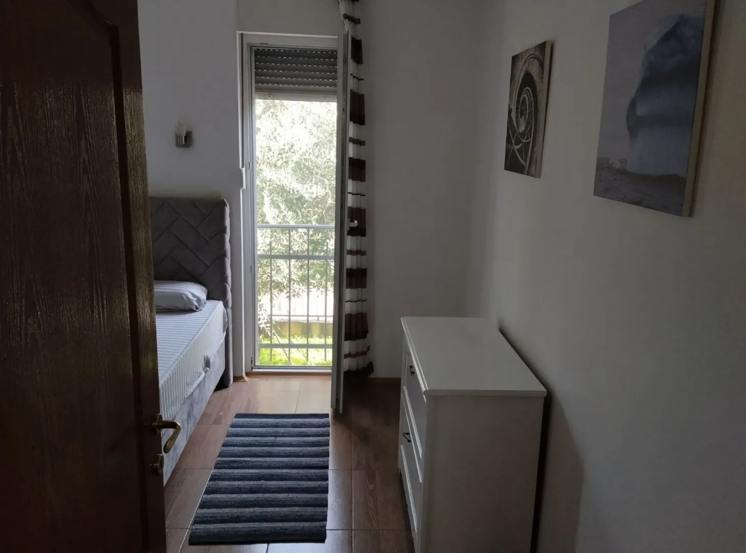 Svijetla spavaća soba sa izlazom na balkon i komodom.