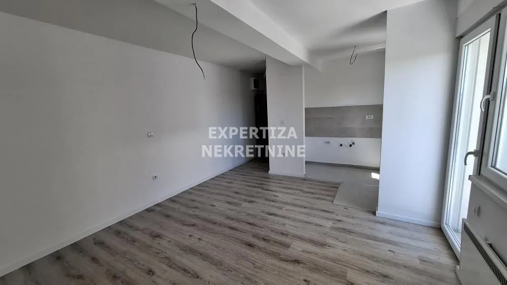 Empty room under construction with installed laminate flooring and a kitchen area.