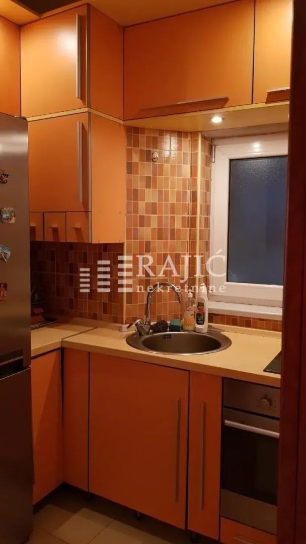 Smaller kitchen with orange cabinets and a sink next to the window.