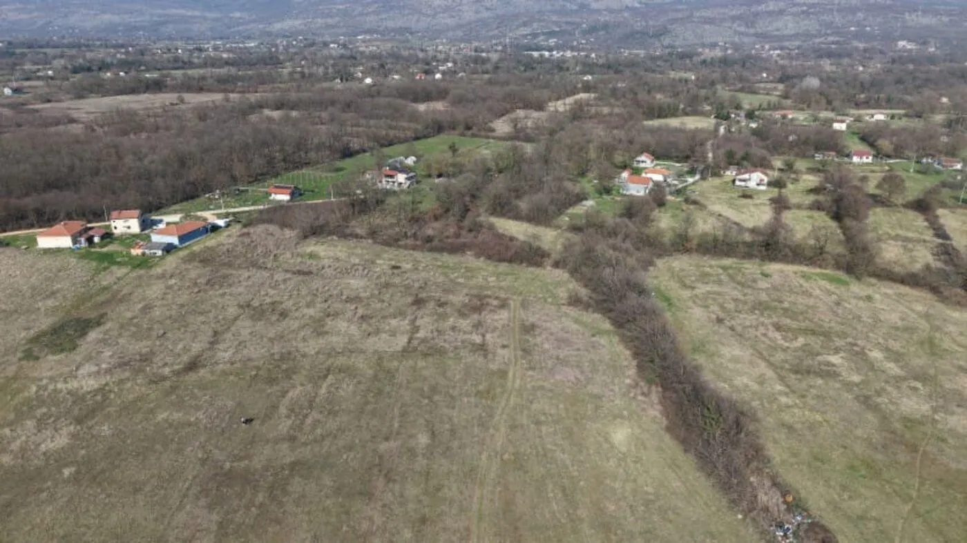 Pogled iz vazduha na zemljište i okolno naselje sa zelenilom.