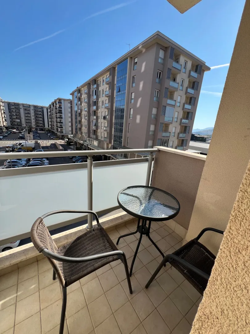 Small furnished balcony with a table and two chairs and a view of buildings.