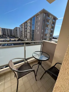 Small furnished balcony with a table and two chairs and a view of buildings. - image 4