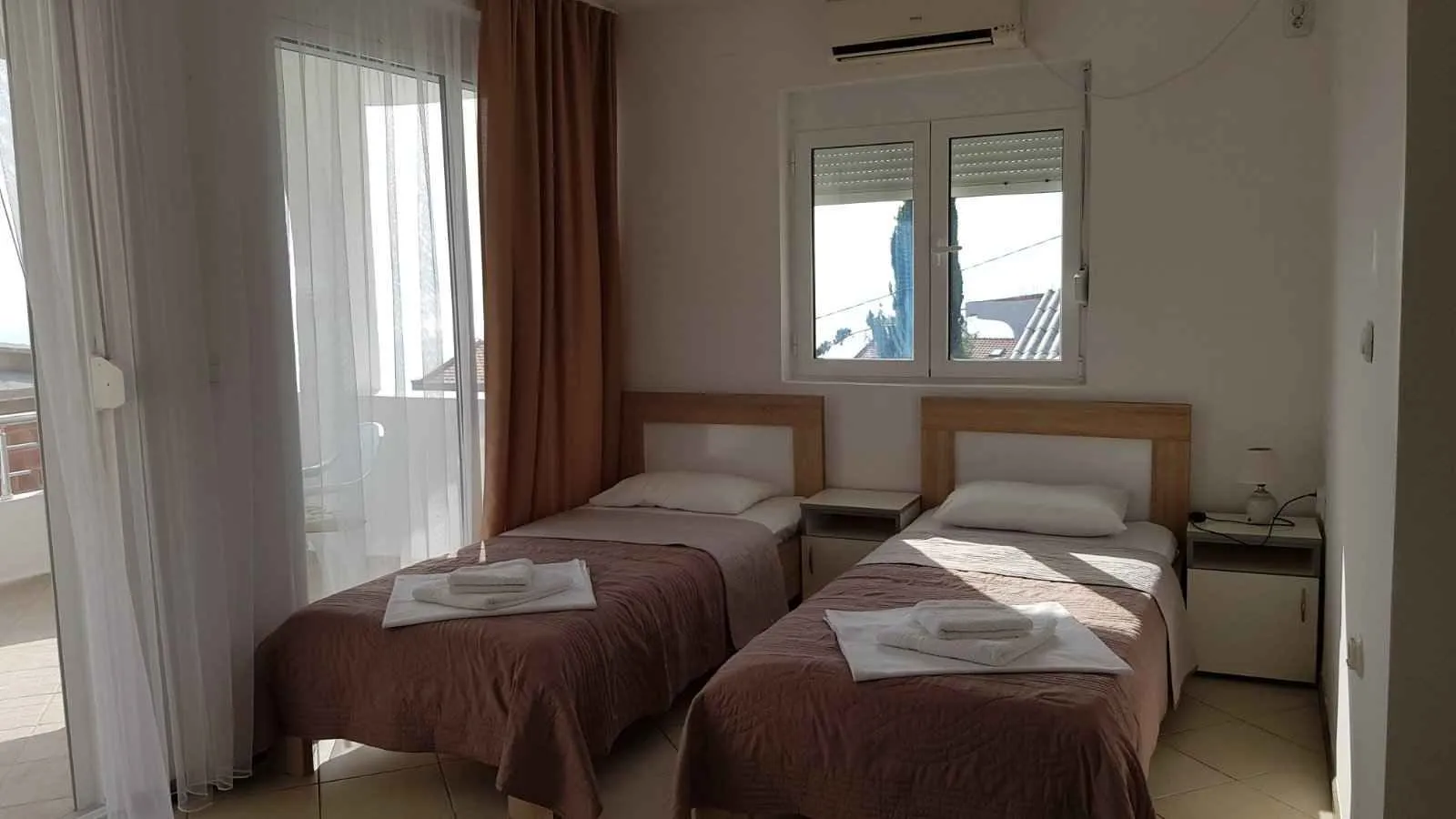 Svijetla spavaća soba sa dva singl kreveta i izlazom na balkon.