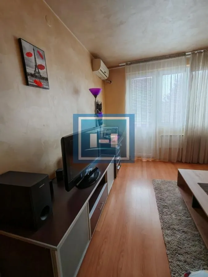 Dnevna soba sa televizorom, nameštajem i prozorom sa zavesama.