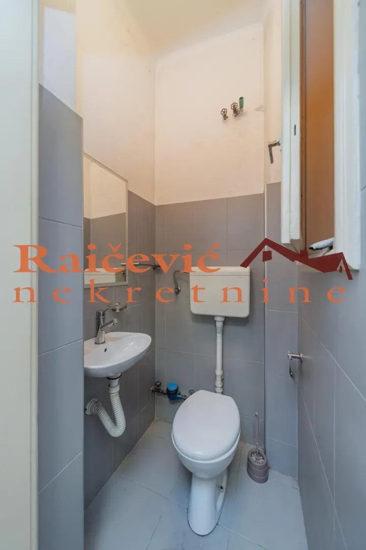 Manje kupatilo sa lavaboom, wc šoljom i sivim pločicama.