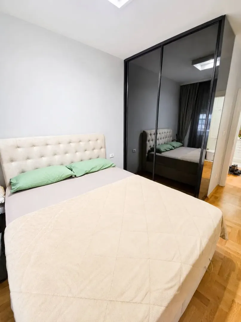 Moderna spavaća soba sa bračnim krevetom i velikim ugradnim garderoberom sa ogledalom.