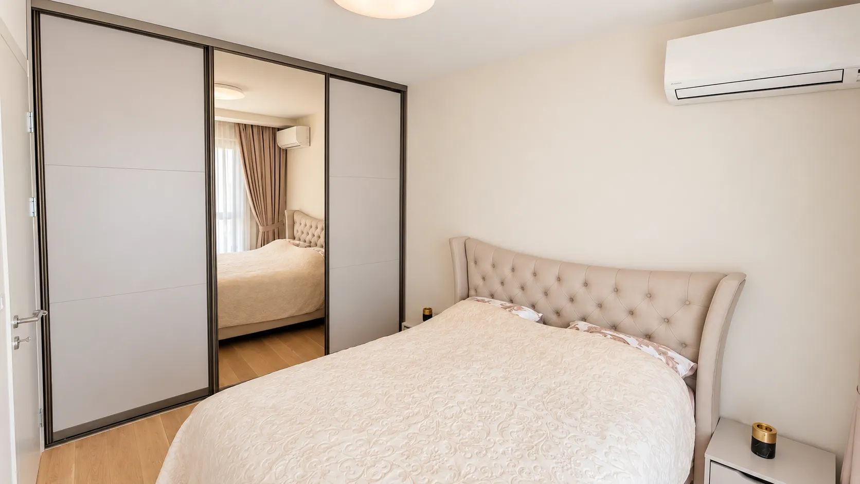 Tidy bedroom featuring a double bed, a large mirrored wardrobe, and an air conditioning unit.