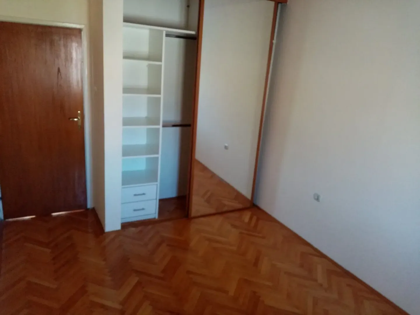 An empty room featuring a built-in wardrobe and parquet floor.