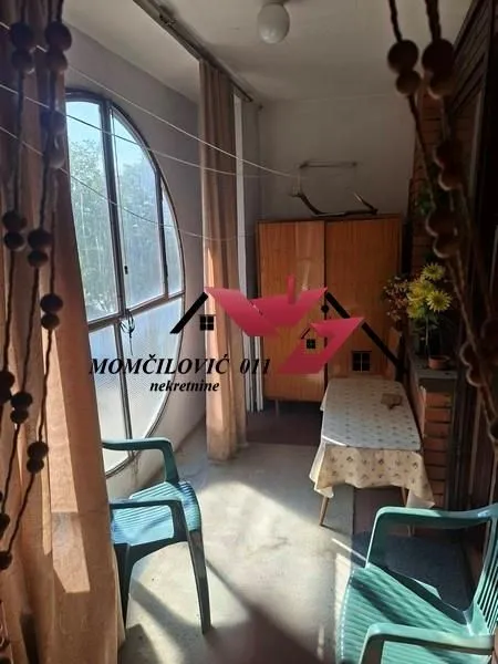 Zastakljeni balkon sa stolom, stolicama i velikim okruglim prozorom.