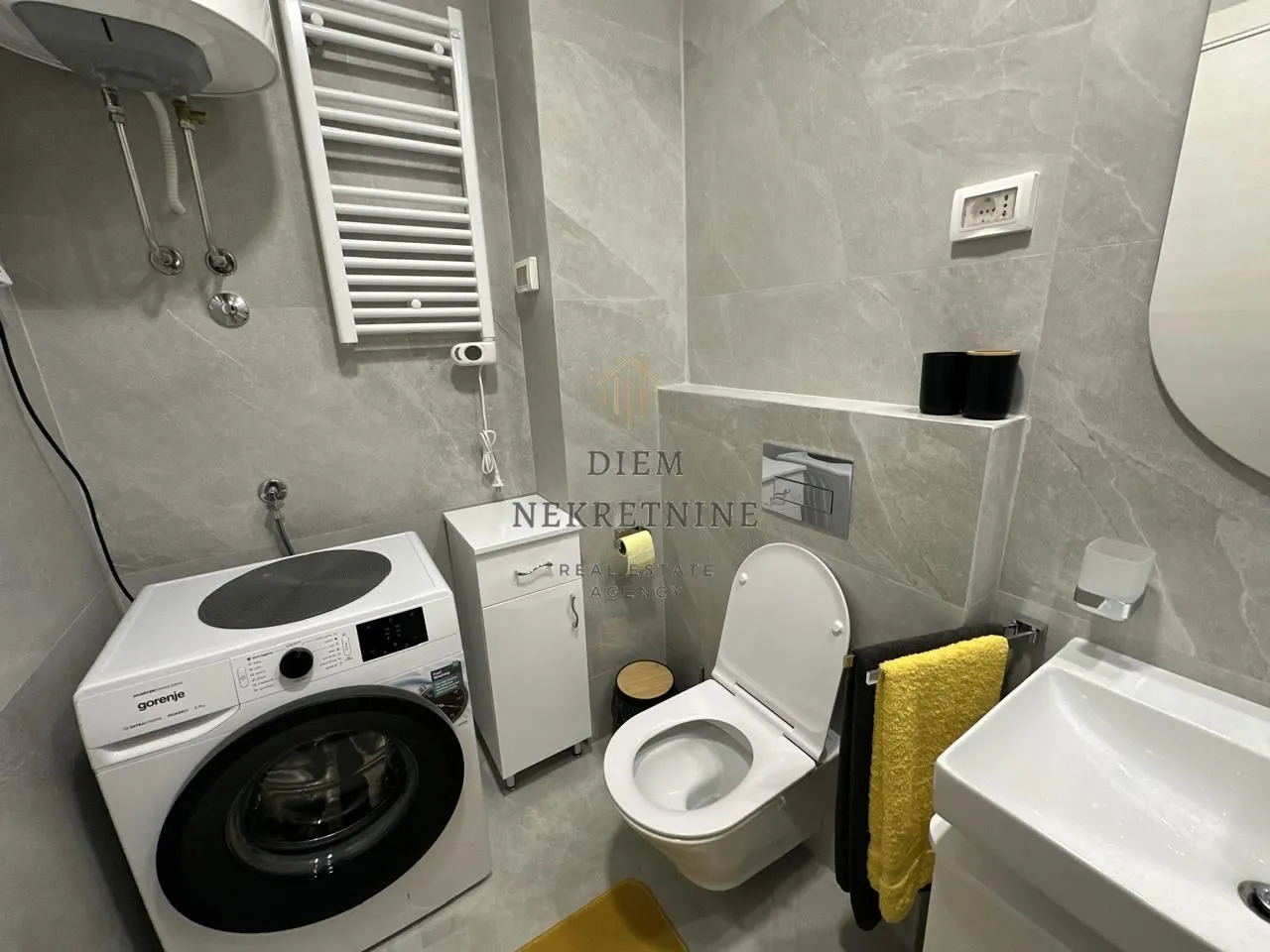 Moderno opremljeno kupatilo sa veš mašinom i sanitarijama.