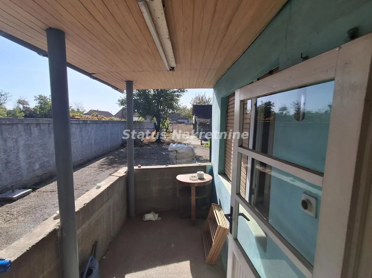 Natkriveni balkon sa pogledom na dvorište i drvenim vratima.